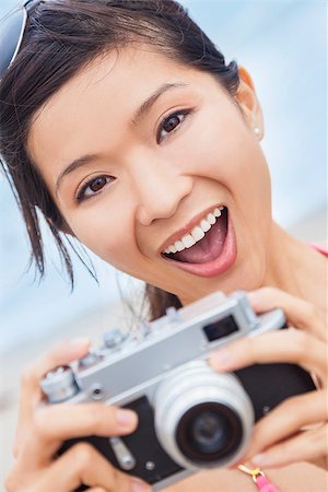 simsearch:400-08291180,k - Happy smiling Chinese Asian young woman or girl in a bikini at the beach taking a photograph using a retro digital camera Foto de stock - Royalty-Free Super Valor e Assinatura, Número: 400-07975539