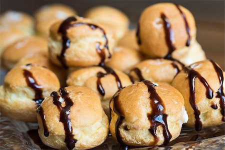 simsearch:400-04835290,k - Looking at a glass plate filled with delicious decadent cream puffs drizzled with chocolate .  Shot on a wood table. Stock Photo - Budget Royalty-Free & Subscription, Code: 400-07976724