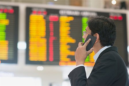 Asian Businessman looking at airport flight timetable and on the phone. Stock Photo - Budget Royalty-Free & Subscription, Code: 400-07978332