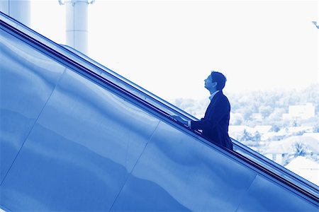 simsearch:400-07978342,k - Asian Indian businessman ascending escalator, side view in blue tone. Photographie de stock - Aubaine LD & Abonnement, Code: 400-07978347