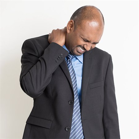 Indian businessman shoulder pain, holding his neck with painful face expression, standing on plain background. Stock Photo - Budget Royalty-Free & Subscription, Code: 400-07989076