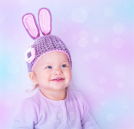 Portrait of happy cute baby girl wearing knitted hat with rabbit ears on purple blur background, beautiful Easter bunny Stock Photo - Budget Royalty-Free & Subscription, Code: 400-07989486