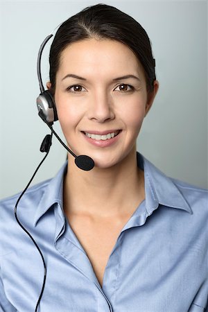 simsearch:400-08293929,k - Attractive female call center operator, client services assistant or telemarketer wearing a headset looking at the camera with a charming friendly smile, on grey with copy space Stock Photo - Budget Royalty-Free & Subscription, Code: 400-07994120