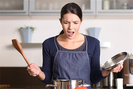 simsearch:862-05997022,k - Young housewife having a calamity in the kitchen reacting in shock and horror as she lifts the lid on the saucepan on the stove to view the contents as she cooks dinner Photographie de stock - Aubaine LD & Abonnement, Code: 400-07993069