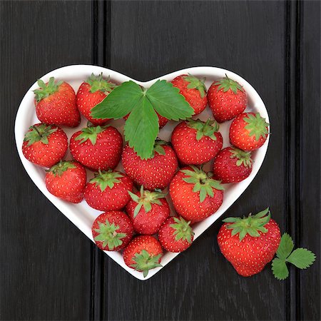 simsearch:400-07993031,k - Strawberry fruit and leaf sprigs in a heart shaped porcelain dish over dark wood background. Foto de stock - Super Valor sin royalties y Suscripción, Código: 400-07993621