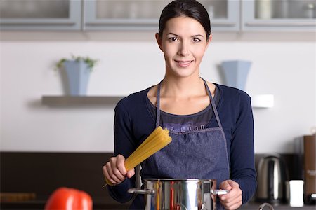 simsearch:614-02049325,k - Young housewife preparing a healthy Italian pasta standing at the stove with a pot full of spaghetti with fresh vegetables in the foreground smiling happily at the camera Foto de stock - Super Valor sin royalties y Suscripción, Código: 400-07993647