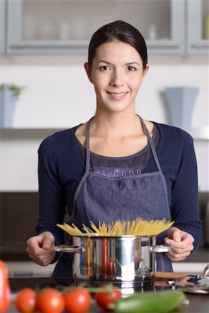 simsearch:614-02049325,k - Young housewife preparing a healthy Italian pasta standing at the stove with a pot full of spaghetti with fresh vegetables in the foreground smiling happily at the camera Foto de stock - Super Valor sin royalties y Suscripción, Código: 400-07993649