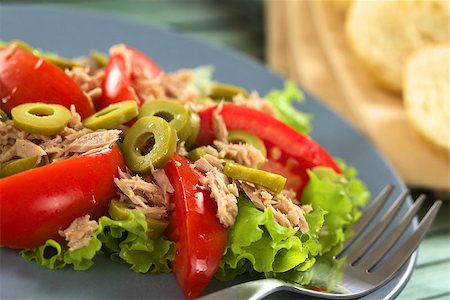 Fresh tuna, tomato and green olive salad served on lettuce leaf on blue plate with fork, baguette slices in the back (Selective Focus, Focus on the front of the olive in the middle of the salad) Stock Photo - Budget Royalty-Free & Subscription, Code: 400-08014888