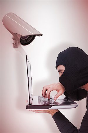 simsearch:694-03328255,k - Focused burglar with balaclava typing on laptop against cctv camera Photographie de stock - Aubaine LD & Abonnement, Code: 400-08019200