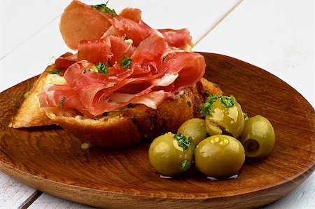 pane all'aglio - Delicious Tapas with Smoked Jamon on Garlic Bread and Heap of Green Olives on Wooden Plate closeup on White Wooden background Fotografie stock - Microstock e Abbonamento, Codice: 400-08011815