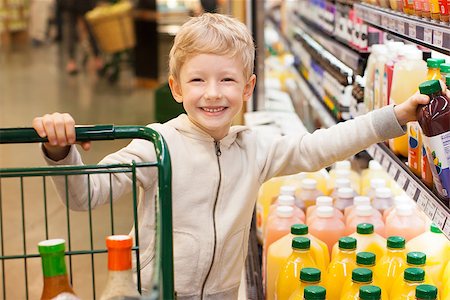 smiling positive boy at the supermarket with shopping cart and choosing juice Foto de stock - Super Valor sin royalties y Suscripción, Código: 400-08036478