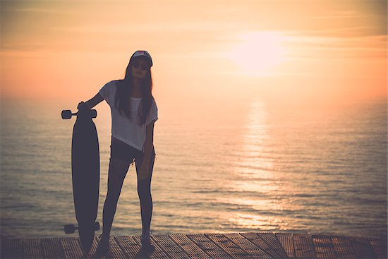 Beautiful fashion skater girl posing with  a skateboard at the sunset Stock Photo - Royalty-Free, Artist: iko, Image code: 400-08033868