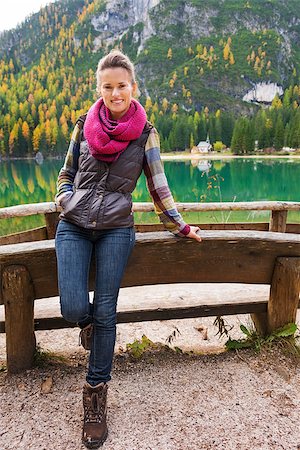 pragser wildsee - A smiling brunette hiker stands facing front, leaning backwards on a wooden railing. The still water in the background provides a perfect mirror image of the mountain and trees. Ideal hiking territory. Stock Photo - Budget Royalty-Free & Subscription, Code: 400-08054028