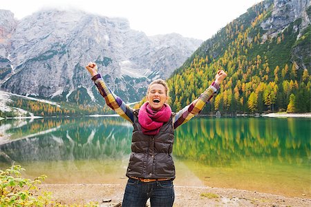 simsearch:400-08054038,k - A happy, smiling woman hiker cheers for joy on the shores of Lake Bries. In the background, the still water reflects the fall colours in the trees, and the Dolomite mountains. The great outdoors. Photographie de stock - Aubaine LD & Abonnement, Code: 400-08054034