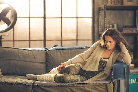 simsearch:400-08054469,k - An elegant brunette woman wearing comfortable, casual clothing, leggings, and a cardigan is relaxing on a sofa in a loft. Sunlight shines through the window. Cozy atmosphere, industrial chic. Stock Photo - Budget Royalty-Free & Subscription, Code: 400-08054458