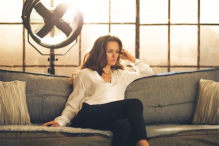 simsearch:400-08054469,k - An elegant brunette is sitting on a sofa in a loft, pensive. In the background, a large window letting in light and an industrial standing fan. Stock Photo - Budget Royalty-Free & Subscription, Code: 400-08054452