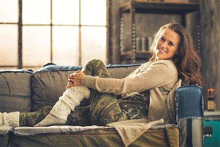 simsearch:400-08054488,k - An elegant brunette smiling woman in comfortable casual clothing, leggings, and a cardigan is relaxing on a loft sofa. Industrial chic ambiance and cozy atmosphere. Stock Photo - Budget Royalty-Free & Subscription, Code: 400-08054460