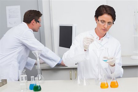 simsearch:400-08055396,k - Scientist pouring chemical fluid in funnel and her colleague working with computer in laboratory Stock Photo - Budget Royalty-Free & Subscription, Code: 400-08054848