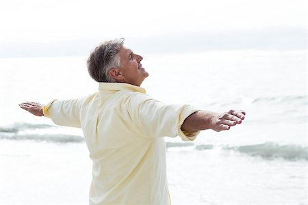 Smiling man standing by the sea arms outstretched at the beach Stock Photo - Budget Royalty-Free & Subscription, Code: 400-08055263