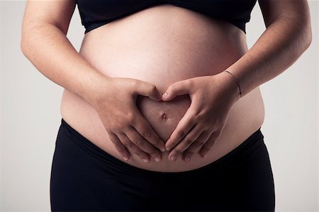 simsearch:400-04859723,k - Pregnant woman showing her belly and making a hearth with hands, over a gray background Fotografie stock - Microstock e Abbonamento, Codice: 400-08075058