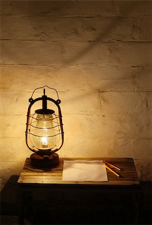 Old fashioned burning kerosene lantern, a blank sheet of paper and two pencils on the old wooden table near old brick wall in the darkness Fotografie stock - Microstock e Abbonamento, Codice: 400-08075127