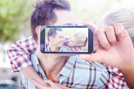 simsearch:400-07664794,k - Hand holding smartphone showing against man giving his pretty blonde girlfriend a piggy back Stock Photo - Budget Royalty-Free & Subscription, Code: 400-08076794