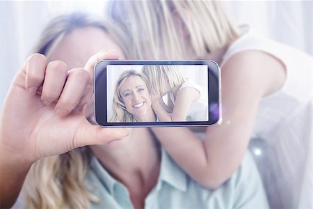 Hand holding smartphone showing against mother sitting with her daughter whispering a secret Stock Photo - Budget Royalty-Free & Subscription, Code: 400-08076854
