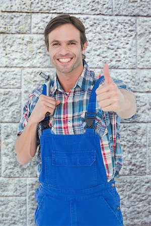 simsearch:400-08077202,k - Confident plumber holding tool while gesturing thumbs up against grey brick wall Foto de stock - Super Valor sin royalties y Suscripción, Código: 400-08077206