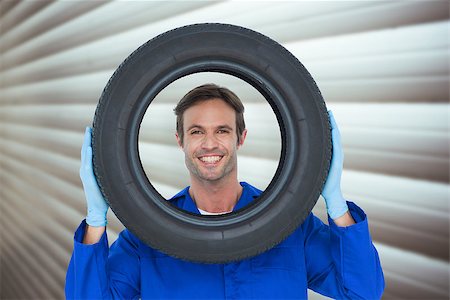 Confident mechanic looking through tire against grey shutters Stock Photo - Budget Royalty-Free & Subscription, Code: 400-08077245