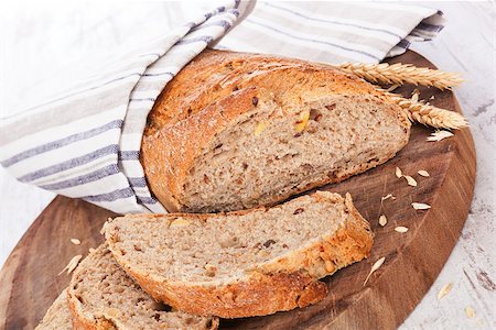 simsearch:400-07996450,k - Dark wholesome bread and slices on round wooden kitchen board on white wooden textured background, rustic styles. Culinary delicious bread eating. Foto de stock - Royalty-Free Super Valor e Assinatura, Número: 400-08072032