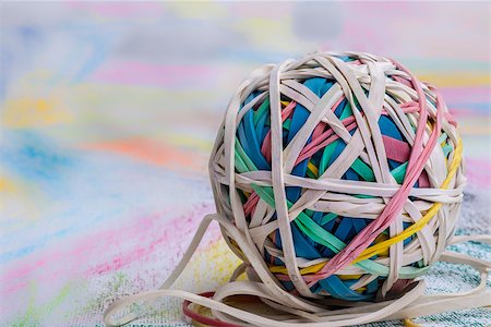 A ball of elastic bands of many different colours placed on a piece of paper that has also been coloured in many different vibrant colours. Photographie de stock - Aubaine LD & Abonnement, Code: 400-08072529