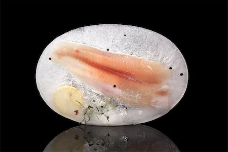 simsearch:400-08070549,k - Culinary seafood eating. Raw fish fillet with lemon, fresh herbs and peppercorns frozen in ice isolated on black background. Luxurious fish eating. Stockbilder - Microstock & Abonnement, Bildnummer: 400-08073409