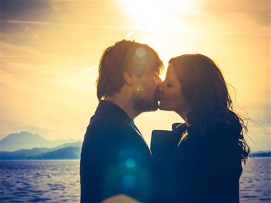 Photo of young adults by the water hugging and kissing in the late afternoon as the sun lowers in the sky. Heavily filtered for more romantic effect. Real lens flare visible. Stock Photo - Royalty-Free, Artist: sumners, Image code: 400-08073656