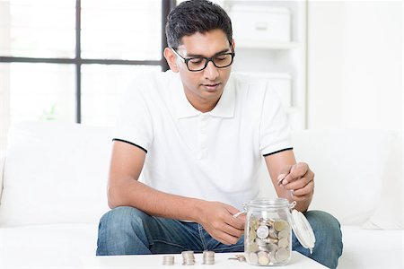 Financial planning concept. Indian guy saving money to glass jar. Asian man sitting on sofa indoor. Handsome male model. Stock Photo - Budget Royalty-Free & Subscription, Code: 400-08114396