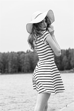 black and white image ,beautiful girl standing near the water on the seaside , she has elegant blue line dress and white hat . looking in camera Photographie de stock - Aubaine LD & Abonnement, Code: 400-08115857