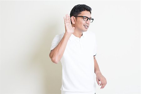 Portrait of Indian guy listening, hand cupped beside ears. Asian man standing on plain background with shadow and copy space. Handsome male model. Stock Photo - Budget Royalty-Free & Subscription, Code: 400-08116550