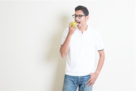 simsearch:400-06457388,k - Man healthcare concept. Indian guy eating a green apple. Asian standing on plain background with shadow and copy space. Handsome male model. Photographie de stock - Aubaine LD & Abonnement, Code: 400-08116572
