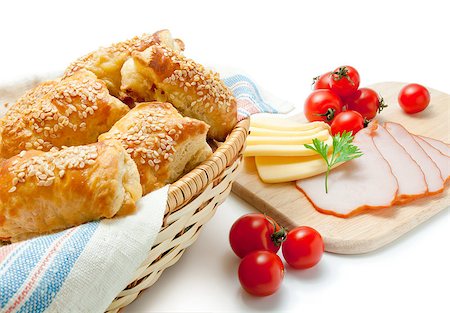 Freshly baked puff pastry patties sprinkled with sesame seeds in a wicker basket closeup arranged with cherry tomatoes cheese ham and parsley isolated on white background. Stock Photo - Budget Royalty-Free & Subscription, Code: 400-08110637