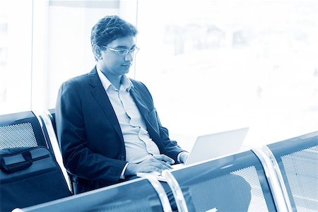 Asian Indian business man waiting his flight at airport, sitting on chair and using laptop, blue tone. Stock Photo - Budget Royalty-Free & Subscription, Code: 400-08111371