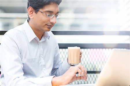 Asian Indian businessman using laptop computer while drinking a cup hot milk tea, outdoor cafe. Photographie de stock - Aubaine LD & Abonnement, Code: 400-08111381
