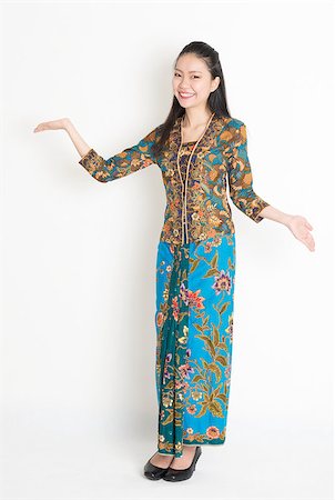 Full length portrait of Southeast Asian woman in batik dress showing welcome gesture standing on plain background. Stock Photo - Budget Royalty-Free & Subscription, Code: 400-08113764