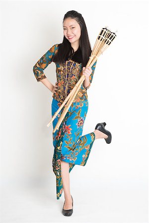 Full body portrait of Southeast Asian woman in batik dress hands holding bamboo oil lamp standing on plain background. Stock Photo - Budget Royalty-Free & Subscription, Code: 400-08113784