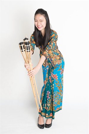 Full body portrait of Southeast Asian woman in batik dress hands holding pelita standing on plain background. Stock Photo - Budget Royalty-Free & Subscription, Code: 400-08113786