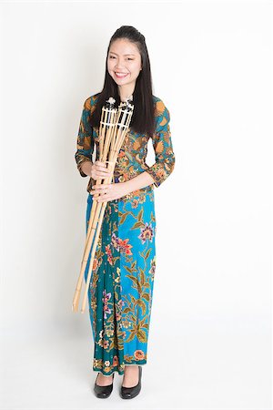 Full body portrait of Southeast Asian girl in batik dress hands holding pelita standing on plain background. Stock Photo - Budget Royalty-Free & Subscription, Code: 400-08113787