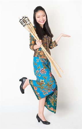 Full body portrait of Southeast Asian woman in batik dress hand holding bamboo oil lamp showing something standing on plain background. Stock Photo - Budget Royalty-Free & Subscription, Code: 400-08113782