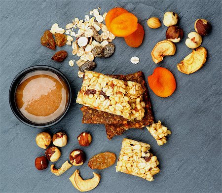 simsearch:400-08152810,k - Arrangement of Useful Granola Bars with Muesli, Nuts, Dried Apricots and Bowl of Honey closeup on Black Stone background. Top View Photographie de stock - Aubaine LD & Abonnement, Code: 400-08154924