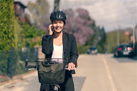 Stylish friendly young businesswoman riding to work pausing to answer a call on her mobile phone standing supporting her bicycle in the road as she chats to her friend Fotografie stock - Microstock e Abbonamento, Codice: 400-08153897