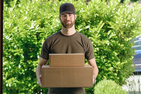 Handsome delivery man or courier with two cardboard boxes in his arms standing waiting to make the door to door delivery at a private house Stock Photo - Budget Royalty-Free & Subscription, Code: 400-08161289