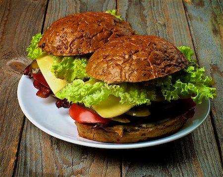 simsearch:400-06330800,k - Homemade Hamburgers with Bacon Lettuce,Tomato, Onions, Cheese, and Pickled Cucumber with Whole Wheat Bun on White Plate closeup on Rustic Wooden background Stock Photo - Budget Royalty-Free & Subscription, Code: 400-08163344