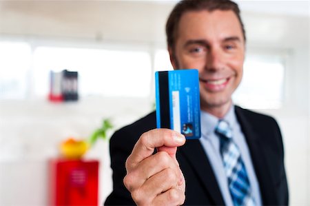 Businessman in formals holding up his credit card and showing to the camera. Stock Photo - Budget Royalty-Free & Subscription, Code: 400-08185786